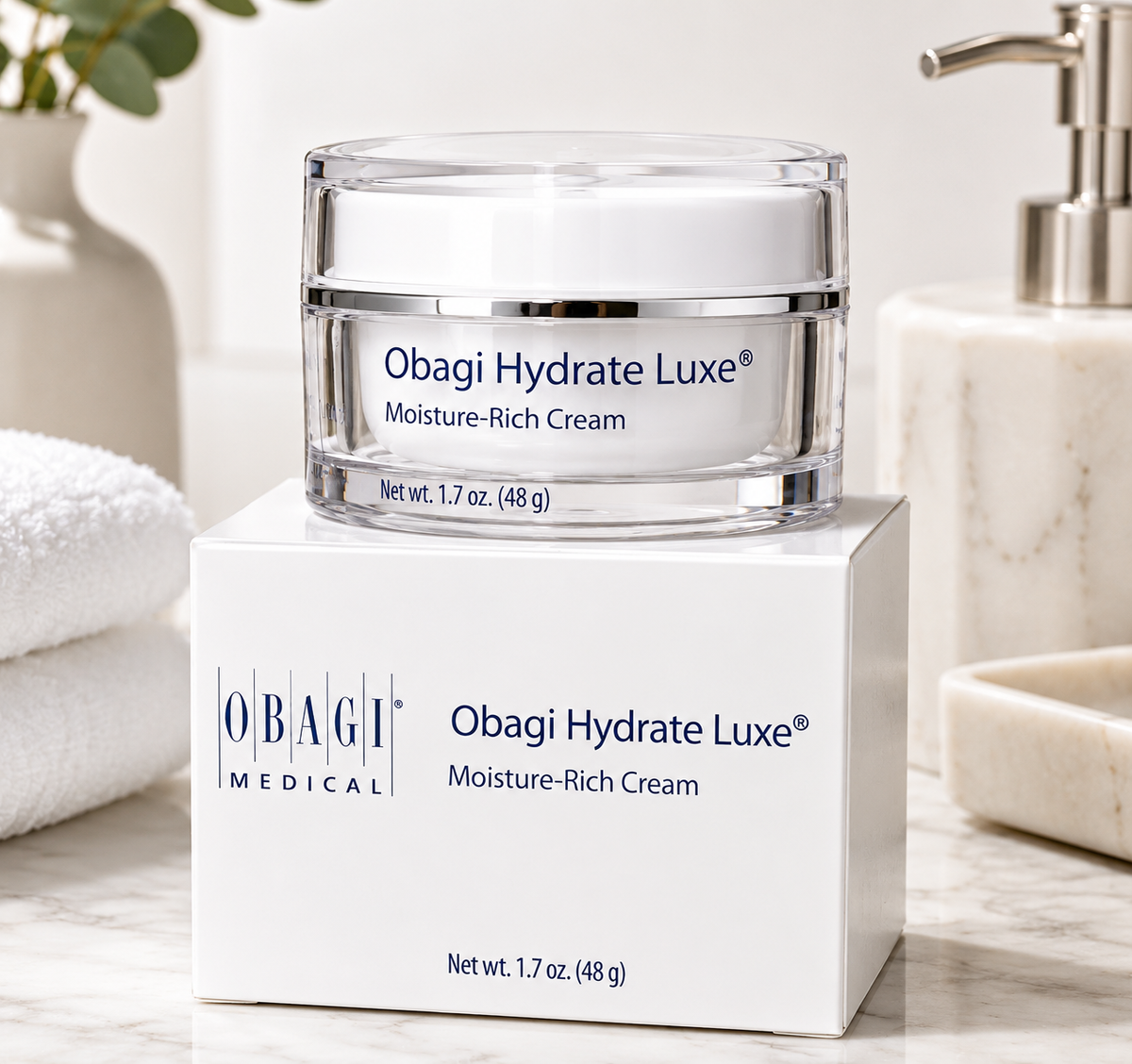 Obagi Hydrate Luxe Moisture-Rich Cream jar on a white box with a bathroom setting.